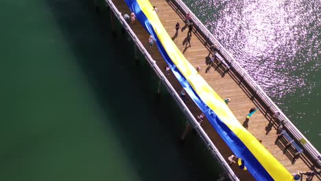 Ukrainische-Demonstranten-Aus-Der-Luft-Mit-Großer-Ukrainischer-Flagge-Protestieren-Gegen-Die-Russische-Invasion-Ihres-Landes-Am-Pier-Von-Malibu,-Kalifornien