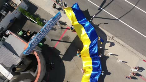 Top-Down-Aerial-Ukrainian-Protesters-With-Large-Ukraine-Flag-Protest-The-Russian-Invasion-Of-Their-Country,-On-The-Street-In-Malibu,-California-With-Malibu-Sign