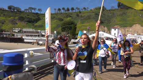 Ukrainische-Antikriegs-Demonstranten-Singen-Und-Marschieren-Auf-Dem-Malibu-Pier-Mit-Schildern-Und-Fahnen,-Um-Gegen-Die-Russische-Invasion-In-Der-Ukraine-Zu-Protestieren