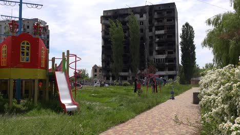 Kids-On-Swings-On-Playground-In-Borodianka,-Borodyanka,-Ukraine-With-Bombed-And-Rocketed-Apartment-Buildings-Where-Hundreds-Were-Killed-By-Russian-Occupation