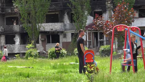 Kids-On-Swings-On-Playground-In-Borodianka,-Borodyanka,-Ukraine-With-Bombed-And-Rocketed-Apartment-Buildings-Where-Hundreds-Were-Killed-By-Russian-Occupation