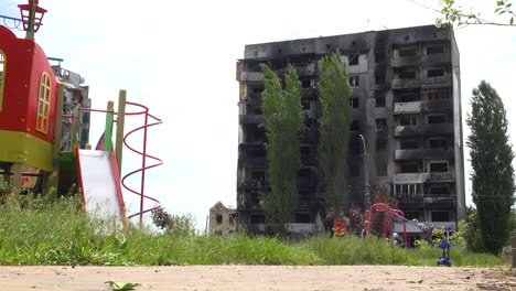 Niños-En-Columpios-En-El-Patio-De-Recreo-En-Borodianka,-Borodyanka,-Ucrania-Con-Edificios-De-Apartamentos-Bombardeados-Y-Disparados-Con-Cohetes-Donde-Cientos-Fueron-Asesinados-Por-La-Ocupación-Rusa