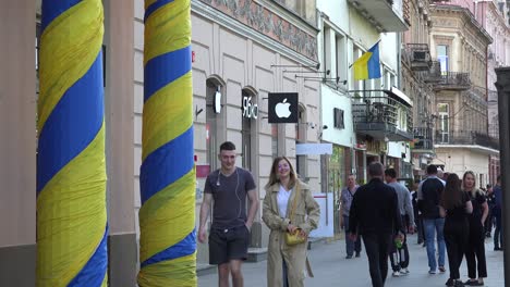 Pedestrians-Walk-On-The-Street-Past-The-Apple-Store-And-Ukrainian-Banners-In-Downtown-Lviv,-Ukraine