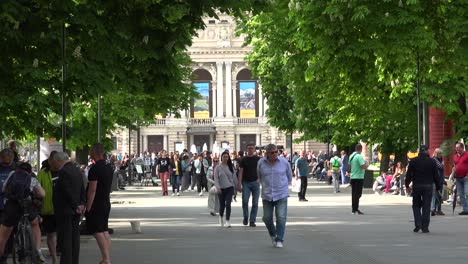 Urban-Crowds-Of-Ukrainians-Walk-Down-Shady-Park-Lane-With-Opera-House-Background-In-Central-Lviv,-Ukraine