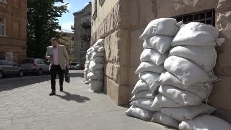 Un-Hombre-De-Negocios-Camina-Por-Una-Calle-En-Lviv,-Ucrania-Con-Sacos-De-Arena-Apilados-Contra-Las-Ventanas-Durante-La-Guerra-En-Ucrania