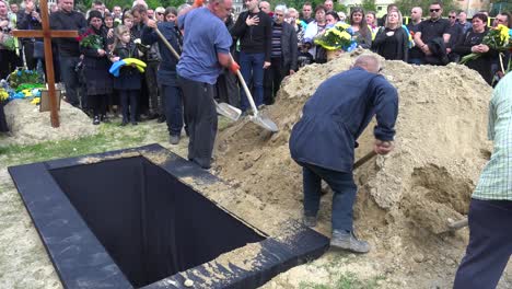 Workers-Shovel-Fresh-Dirt-In-An-Open-Grave-At-A-Cemetery-In-Lviv,-Ukraine-During-A-Soldier-Funeral