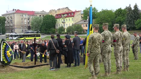 Soldiers-Look-On-As-Workers-Shovel-Fresh-Dirt-In-An-Open-Grave-At-A-Cemetery-In-Lviv,-Ukraine-During-A-Ukrainian-War-Soldier-Burial-Funeral