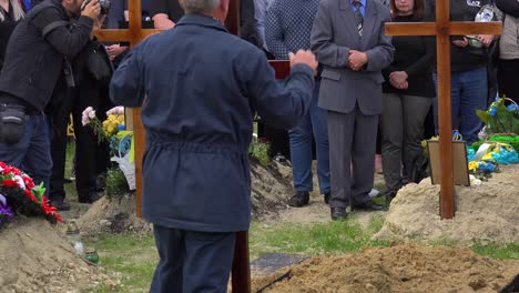 A-Christian-Cross-Marks-The-Gravesite-Of-A-Fallen-Ukrainian-Soldier-During-The-War-In-Ukraine,-The-Family-Looks-On