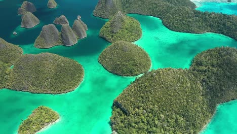 Excellent-Aerial-Shot-Of-The-Wayag-Islands,-Raja-Ampat,-Indonesia,-With-The-Shadows-Of-Passing-Clouds-Visible-In-The-Clear-Blue-Water