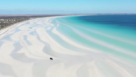 Excelente-Toma-Aérea-De-Una-Camioneta-Conduciendo-Por-Las-Arenas-Blancas-De-La-Playa-Flaherty-Cerca-De-Aguas-Azules-Claras