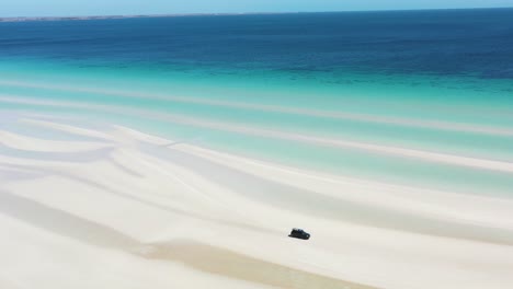 Ausgezeichnete-Luftaufnahme-Eines-Lieferwagens,-Der-Entlang-Des-Weißen-Sandstrandes-Des-Flaherty-Strandes-In-Der-Nähe-Des-Klaren-Blauen-Wassers-Fährt