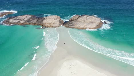 Excelente-Toma-Aérea-De-Un-Turista-Parado-Entre-Arena-Blanca-Y-Surf-Azul-Claro-En-Wylie-Bay,-Esperance,-Australia