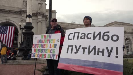 Two-Male-Political-Demonstrators-Carry-A-Sign,-One-In-Russian-Language,-Protesting-President-Elect-Donald-Trump