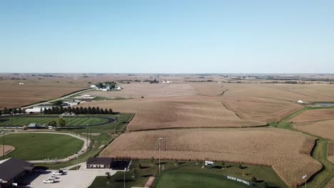 Aerial-Drone-Footage-Of-High-School-Football-Field-And-Tall-Brown-Fields-Ready-For-Harvest-In-Rural,-Midwest-Iowa-Corn-Country