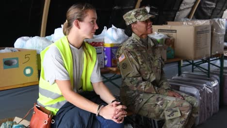 Female-Soldier-And-Red-Cross-Personnel-Planning-Session-About-Distributing-Food-And-Infant-Supplies,-Operation-Allies-Refuge