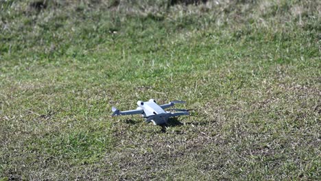 a-drone-lands-on-a-grassy-ground,-filmmaking-gear-with-propellers