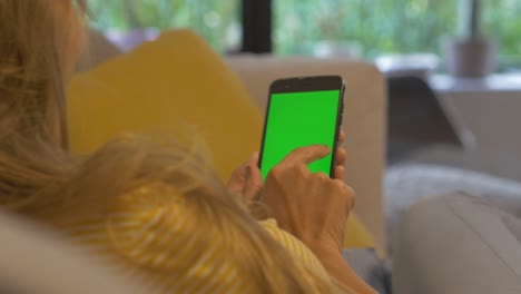 Mädchen-Wischt-über-Ihr-Smartphone,-Während-Sie-Auf-Der-Couch-Sitzt,-Grüner-Bildschirm,-Chroma-Key