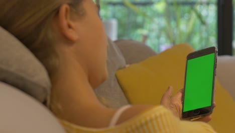 Close-up-woman-holding-smartphone-green-screen-while-chilling-on-the-Couch