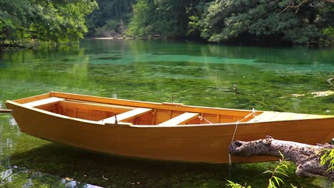 Kleines-Holzboot,-Das-Auf-Der-Oberfläche-Eines-Ruhigen,-Unberührten,-Kristallklaren,-Reflektierenden-Wassers-Schwimmt