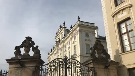 Royal-wrought-iron-gate-with-art-details-and-decorative-facade-sculptures-in-the-background