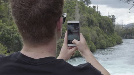 Eine-über-die-schulter-aufnahme-Von-Jemandem,-Der-Mit-Einem-Telefon-Fotos-Von-Den-Huka-fällen-In-Taupo,-Nz-Macht