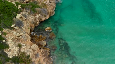 AERIAL-DOLLY-IN:-Drone-flying-over-rock-formations-in-Calamosche-beach,-in-the-Vendicari-Reserve,-a-seaside-paradise-of-Sicily,-Italy,-tilt-up-shot