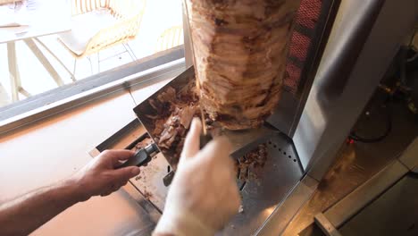 Wide-angle-shot-of-a-man-slicing-meat-on-a-vertical-rotisserie-in-slow-motion-wearing-glove,-fast-food-meal