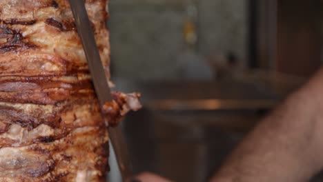 Close-up-of-stacked-meat-grilled-and-cut-on-vertical-rotisserie-spinning-by-a-man-in-slow-motion