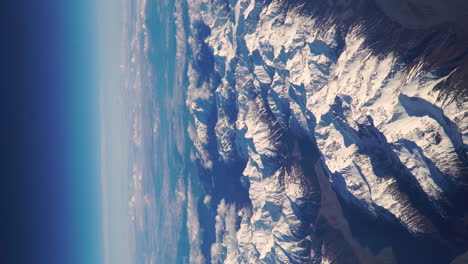 Vista-Vertical-Desde-La-Ventana-Del-Avión-Sobre-Montañas-Nevadas