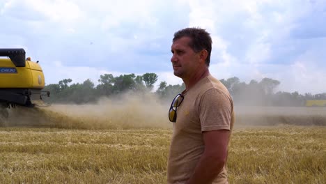 A-wheat-farmer-looks-at-a-combine-harvester-harvesting-wheat-crop-fields-during-the-summer-in-Ukraine