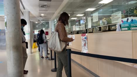 People-with-masks-waiting-in-line-in-front-of-a-hospital-reception-desk