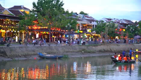 Turistas-En-Pequeños-Botes-Con-La-Ciudad-Antigua-De-Hoi-An-En-El-Fondo-Llena-De-Turistas