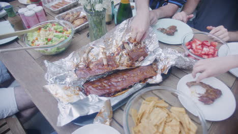 Vista-Aérea-De-Las-Manos-Metiéndose-En-Costillas-Cocidas-A-La-Barbacoa-En-La-Mesa