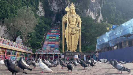 Bandada-De-Palomas-Caminando-Y-Volando-En-Busca-De-Comida-Del-Suelo-En-El-Famoso-Templo-Hindú-De-Las-Cuevas-De-Batu-En-Selangor,-Kuala-Lumpur,-Malasia