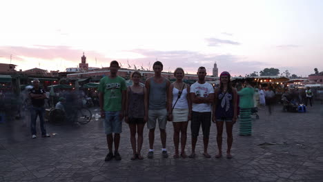 Grupo-De-Turistas-De-Pie-Para-Tomar-Fotografías-En-La-Plaza-Del-Mercado-En-Marrakech,-Marruecos-Al-Atardecer