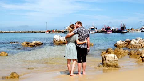 Una-Pareja-Joven-Y-Romántica-Se-Abraza-Descalza-En-El-Cálido-Océano-De-Sudáfrica-Viendo-Los-Barcos-Del-Puerto-De-La-Bahía-De-Kalk