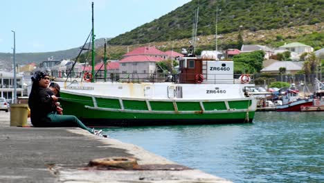 Casual-contented-couple-sitting-on-Kalk-Bay-harbour-wall-relaxing-fishing