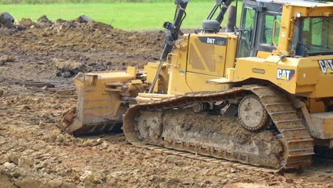 Side-view-of-D6T-Dozer-pushing-heavy,-wet-dirt-to-prepare-a-site-for-a-new-pond