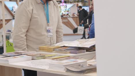 Half-body-shot,-male-smiling-facing-kiosk-at-tourism-event,-overlooking-brochures