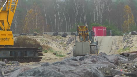 Sitio-De-Construcción-En-La-Costa-Del-Mar-Báltico,-Reforzando-La-Costa-Del-Mar-Báltico,-Construyendo-Un-Muelle-De-Piedra-Protector,-Transportador-Amarillo-Pesado-Que-Entrega-Grandes-Bloques-De-Hormigón,-Día-Nublado