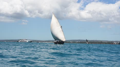 Dhow-sailboat-navigating-among-other-ships-near-the-coastline,-Wide-angle-shot