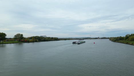 Aerial-Dolly-Towards-Stern-Of-Virage-Cargo-Ship-Travelling-Along-Oude-Maas-With-Barge-Carrying-Cargo-Containers