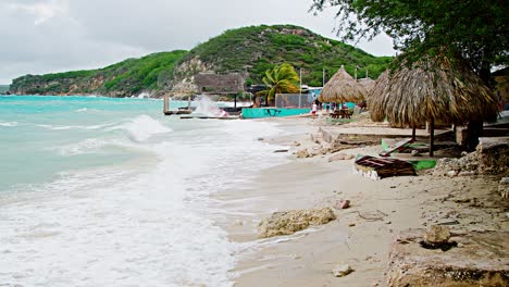 Wide-pan-reveal-of-local-wooden-fishing-boat-being-smashed-into-land-during-sudden-storm-with-rough-waves,-Caribbean