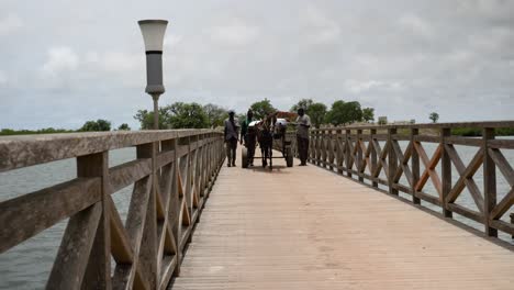 Three-men-and-a-donkey-pulled-cart-carrying-food-sacks-cross-the-bridge-towards-the-Fadiouth-island,-Senegal