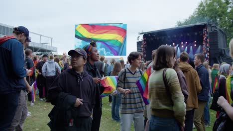 Group-of-friends-talk,-dance-and-sing-in-Oslo-Pride-2022,-handheld-side-view