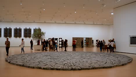 Escultura-Del-Círculo-De-Bilbao-Por-Richard-Long-Dentro-Del-Museo-Guggenheim-Con-Gente-Caminando-Alrededor-De-él,-Tiro-Amplio-Y-Estable