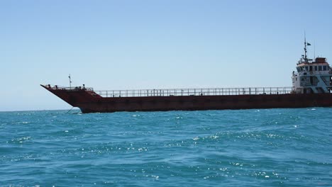 Transportation-ship-with-rusty-pain-sailing-in-the-Indian-Ocean-near-the-East-African-coast,-View-from-small-boat