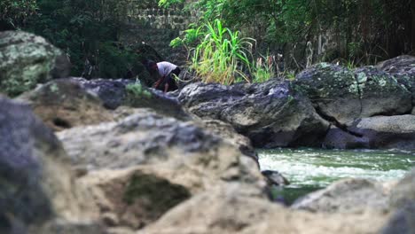 Asiatischer-Mann,-Der-Während-Des-Sonnigen-Tages-Fische-Auf-Felsigem-Fluss-In-Der-Natur-Sucht-Und-Fängt