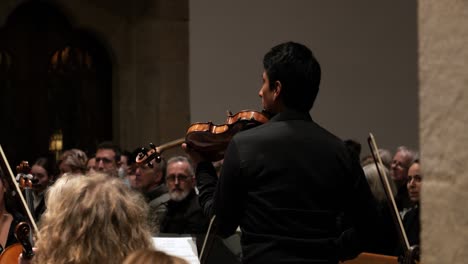 Toma-Manual-En-Cámara-Lenta-Media-De-Una-Orquesta-Durante-Un-Concierto-Con-Violinistas-Tocando-El-Réquiem-De-Mozart-Mientras-Los-Visitantes-Escuchan-El-Sonido