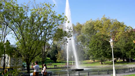 Tall-waterspout-fountains-and-main-pond-in-Doña-Casilda-Park-with-couple-taking-pictures,-Wide-angle-shot